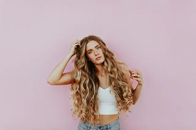 service-partial-highlights-female-dark-blonde-with-long-curly-hair-against-back-of-pink-wall-641x428