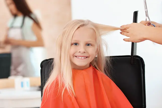 female hairdresser working with little blonde girl sitting in chair in salon closeup of little girl 645x430