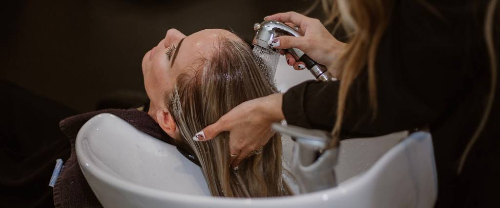 female-hairstylist-washing-blone-female-customers-hair-in-white-hair-wash-bowl