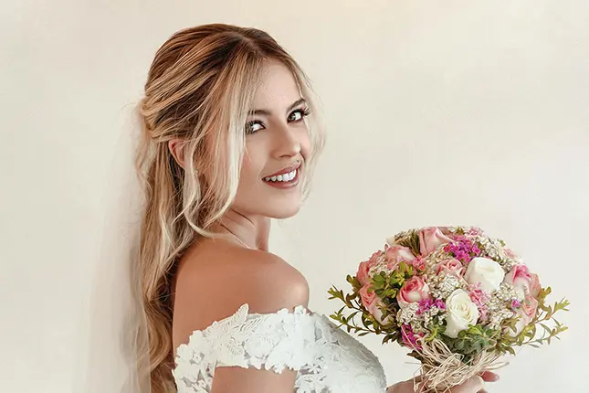blonde-bride-smiling-holding-flowers-looking-at-camera-in-lace-wedding-dress